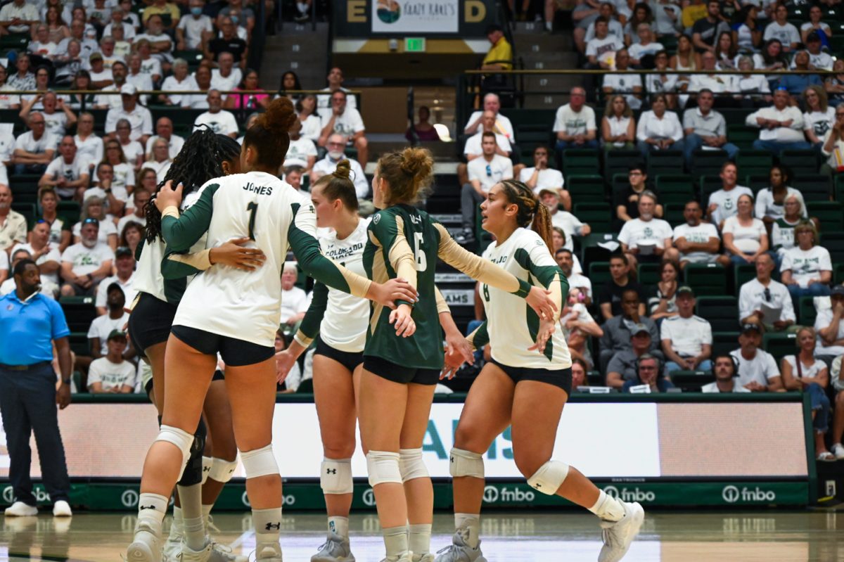 CSU volleyball team dressed in white and green long sleeve uniforms and black shorts hug on the court in front of a large crowd