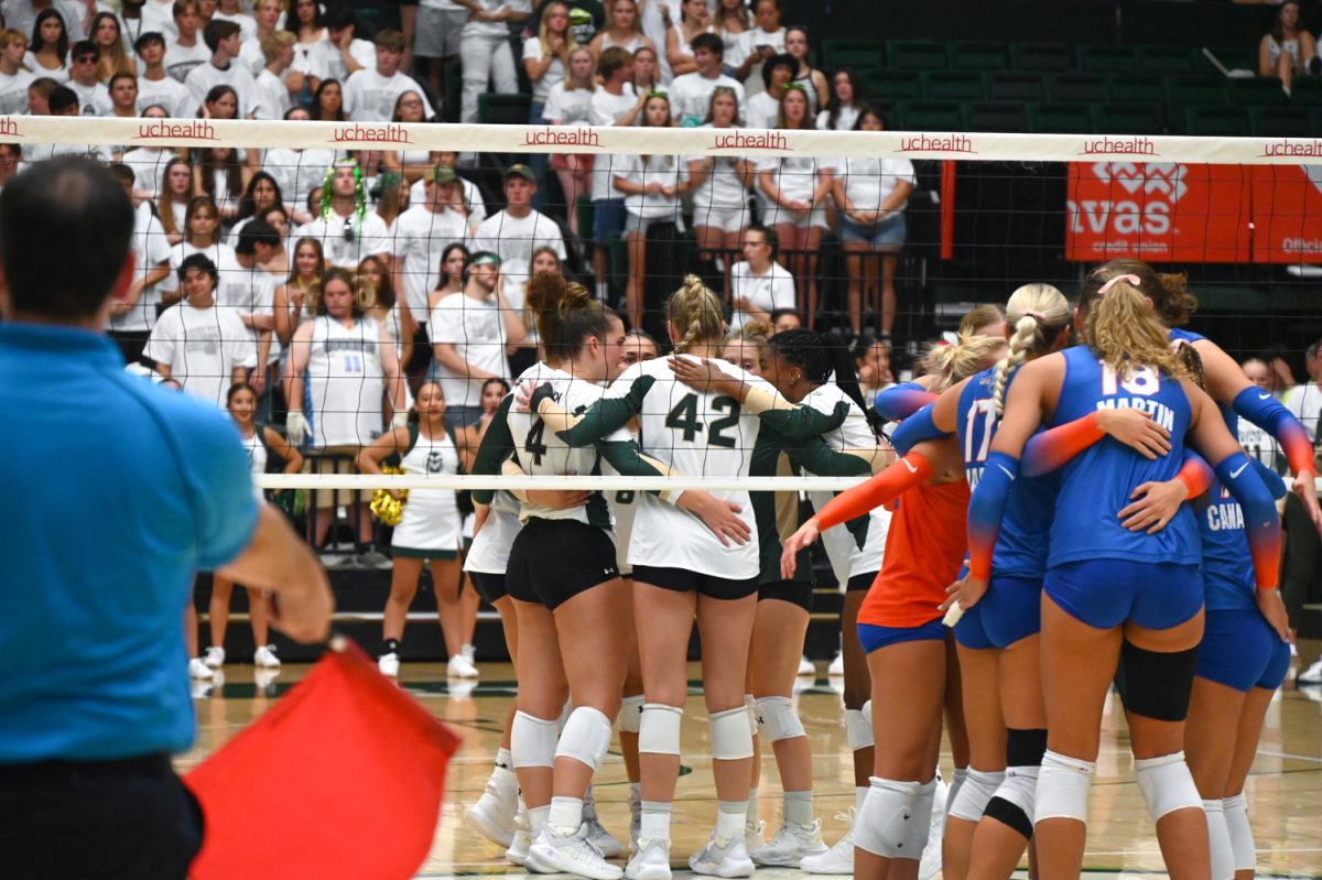 Colorado state's volleyball team, dressed in green and white huddles on the court as well as the opposing team, Florida dressed in blue and orange sleeveless uniforms huddles on the court. both on opposite sides of the net