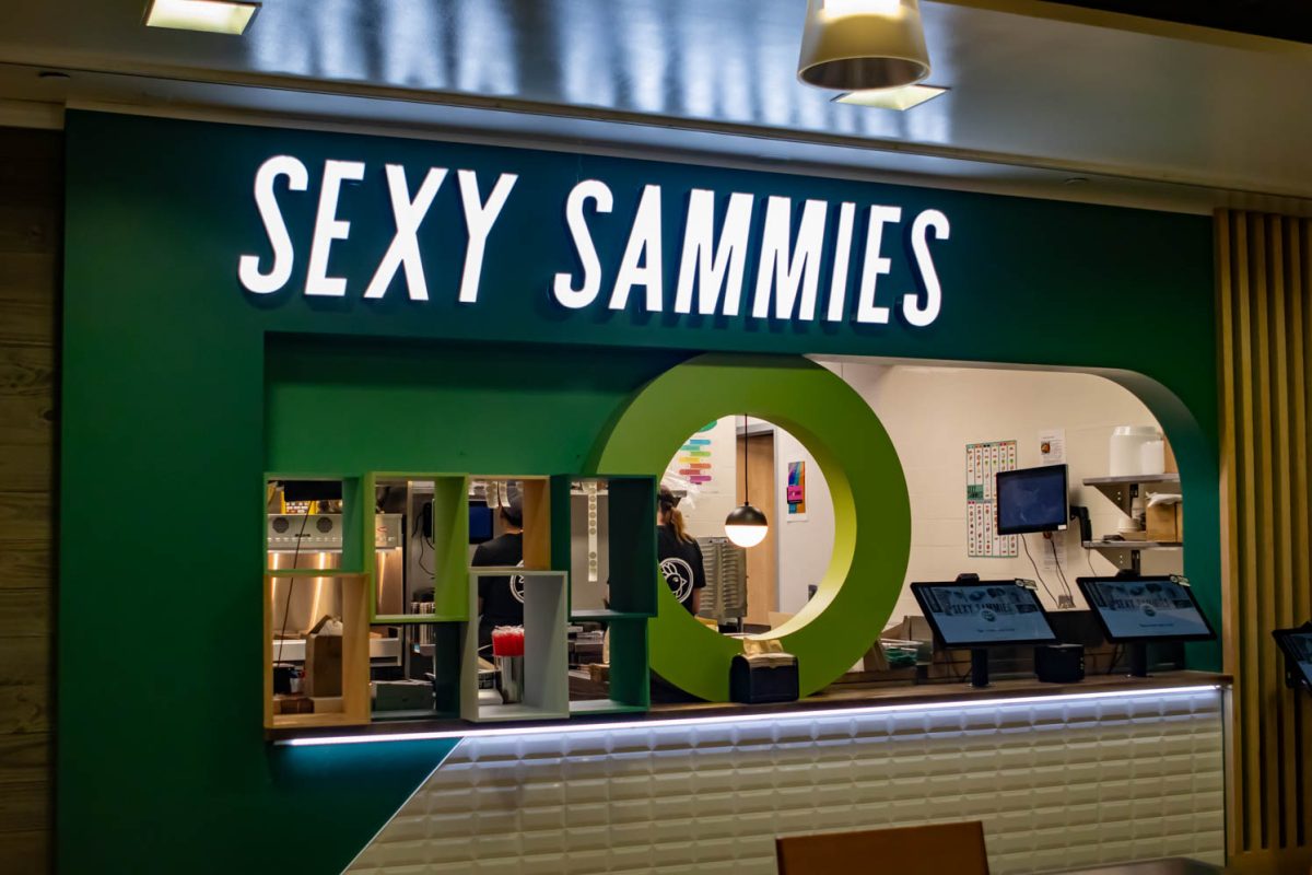 A sandwich shop counter with a green and white sign reading, sexy sammies.