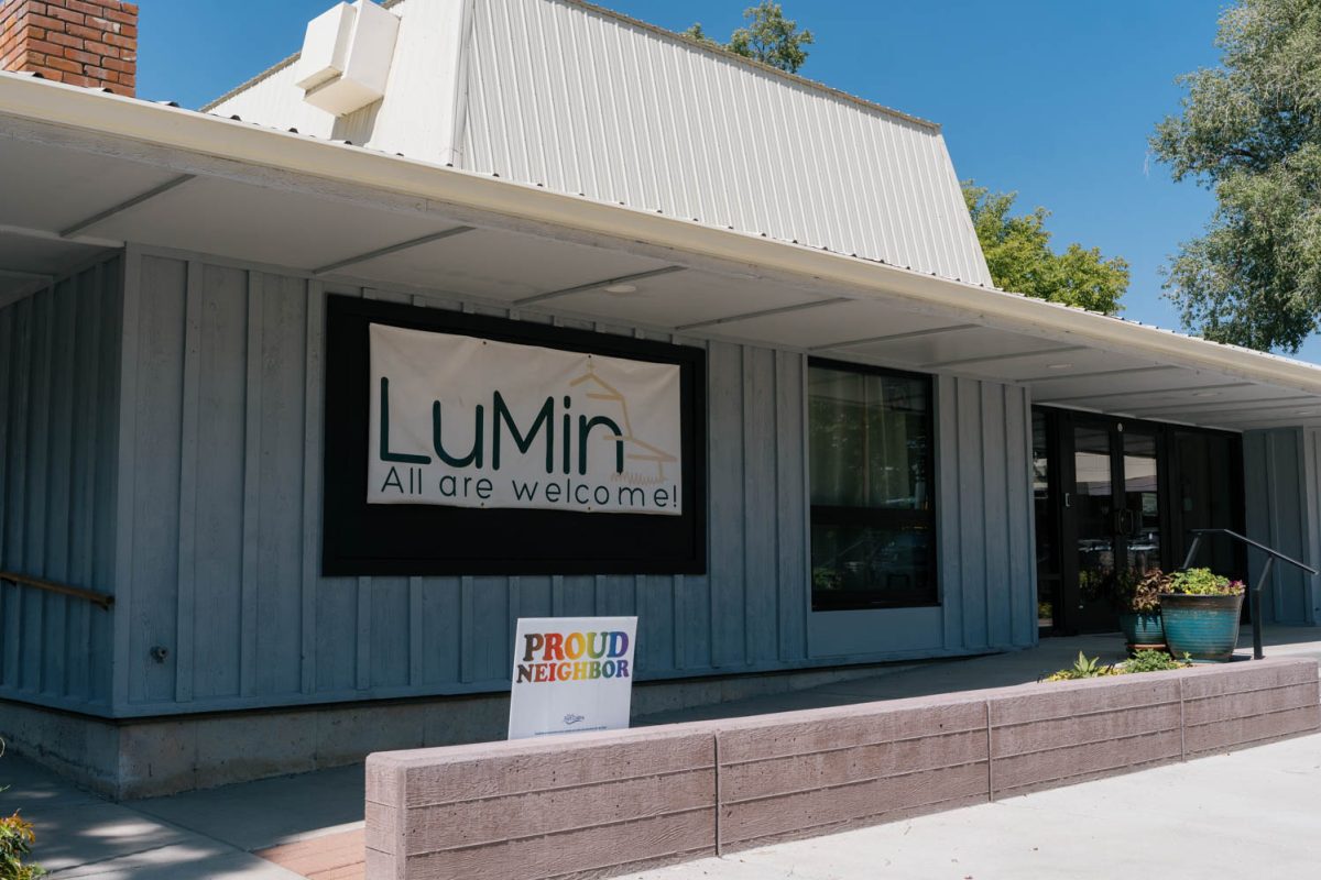 A grey and white church building with brick planters and a banner on the building that says, "LuMin All are welcome."