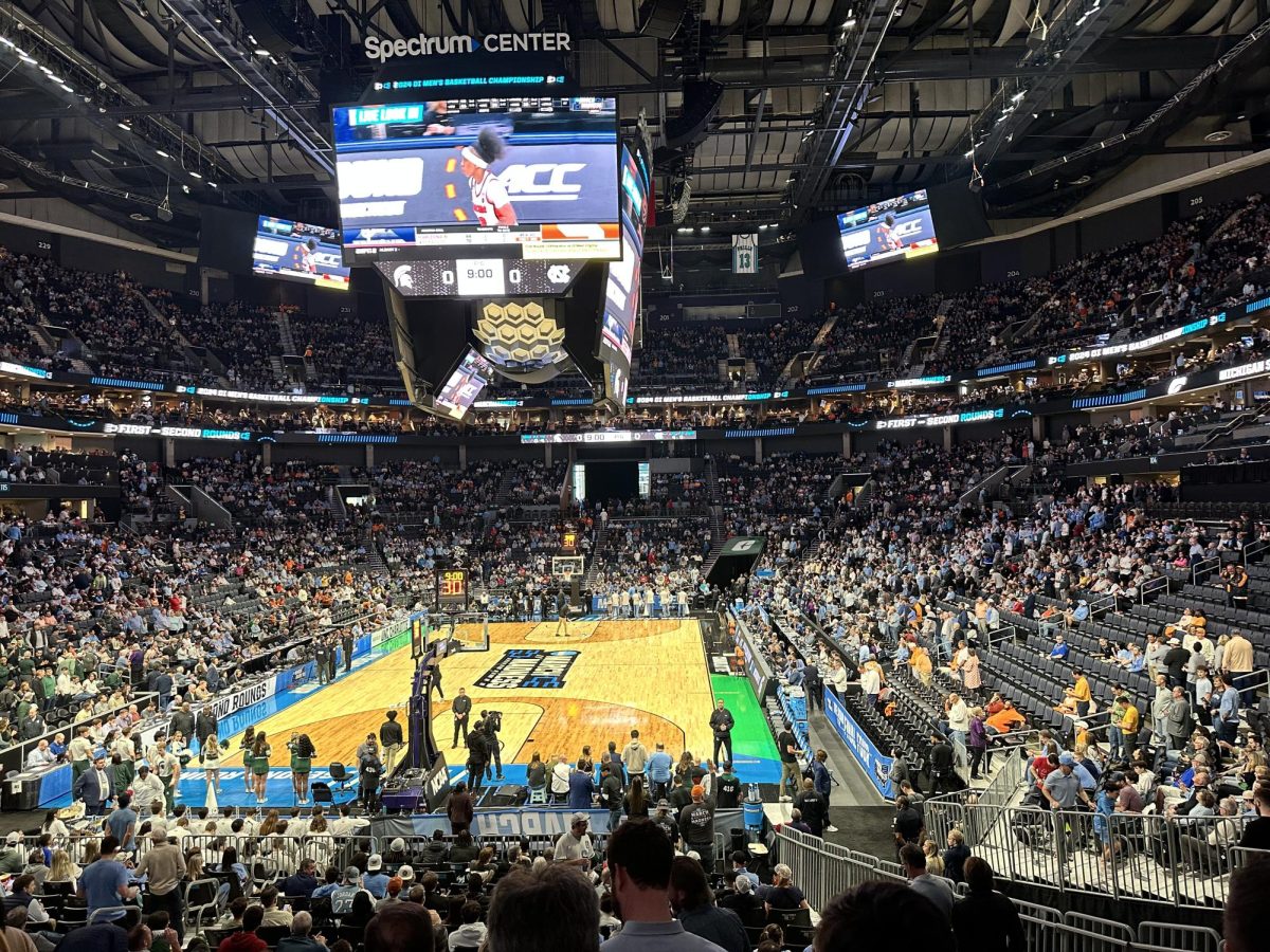 A crowded sports arena ahead of the beginning of the basketball game, with a jumbotron projecting an Atlantic Coast Conference basketball advertisement.