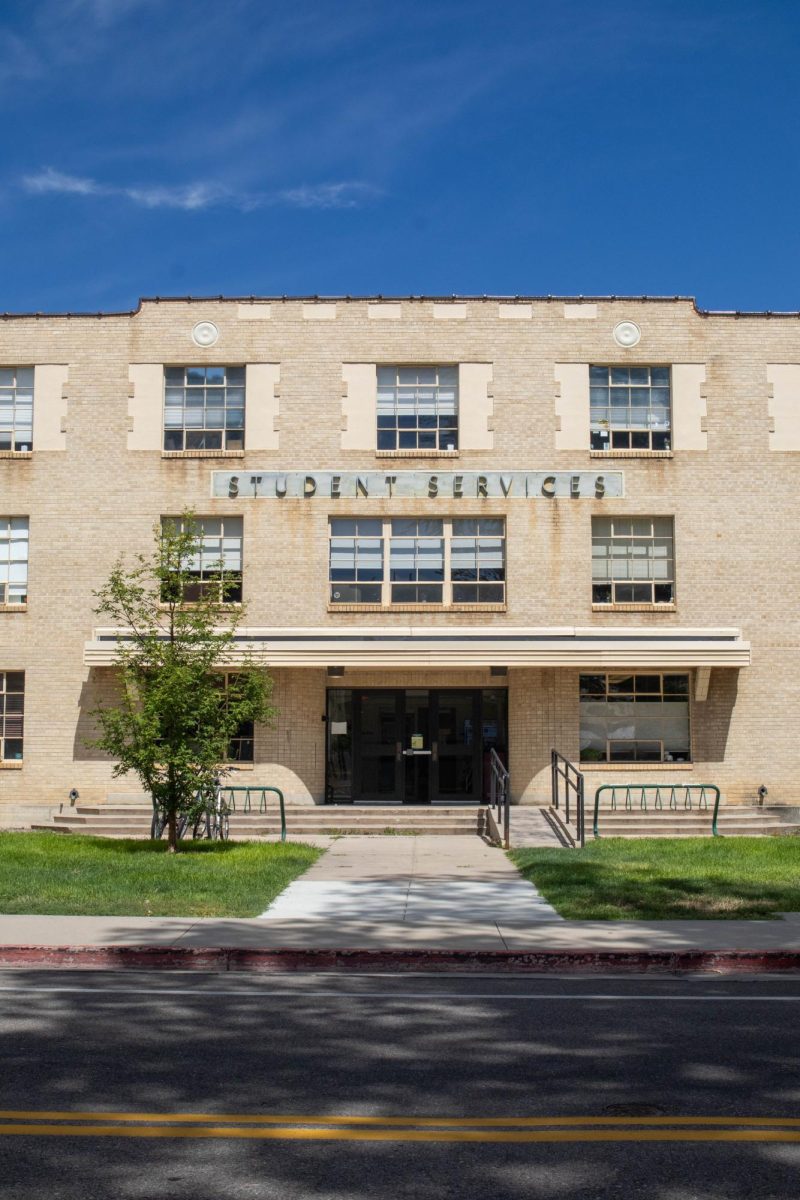A three story tall brick building stands atop green grass. The building has letters that read Student Services in all capital letters.