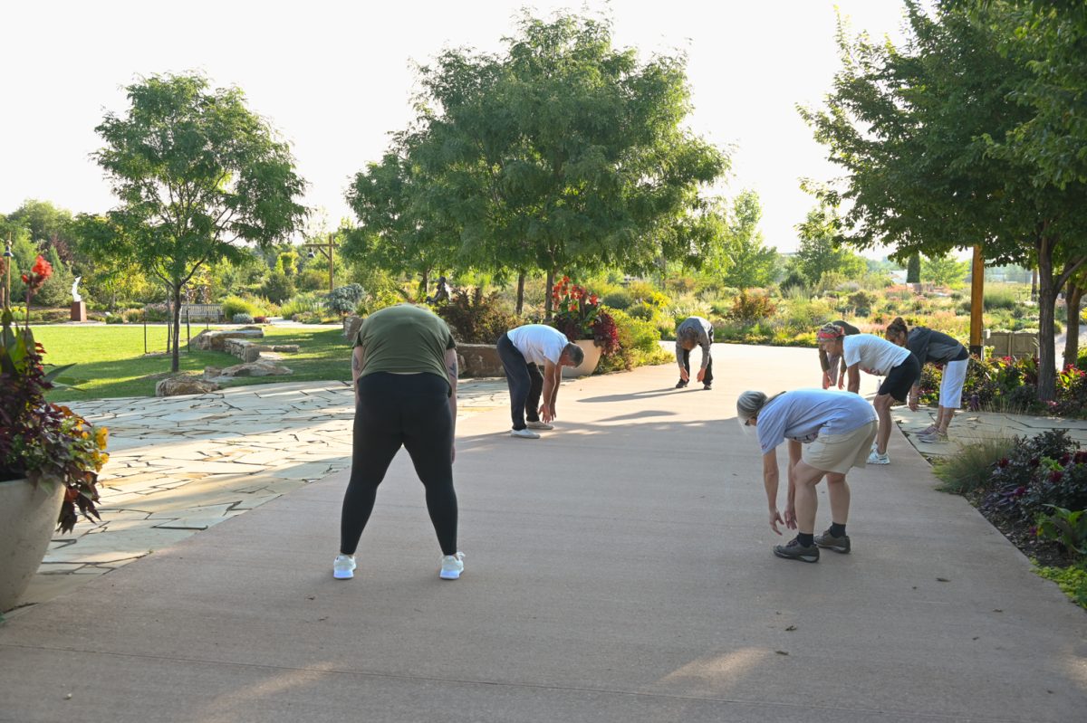 A small group of people lean down and touch their toes in the early morning in a flower garden