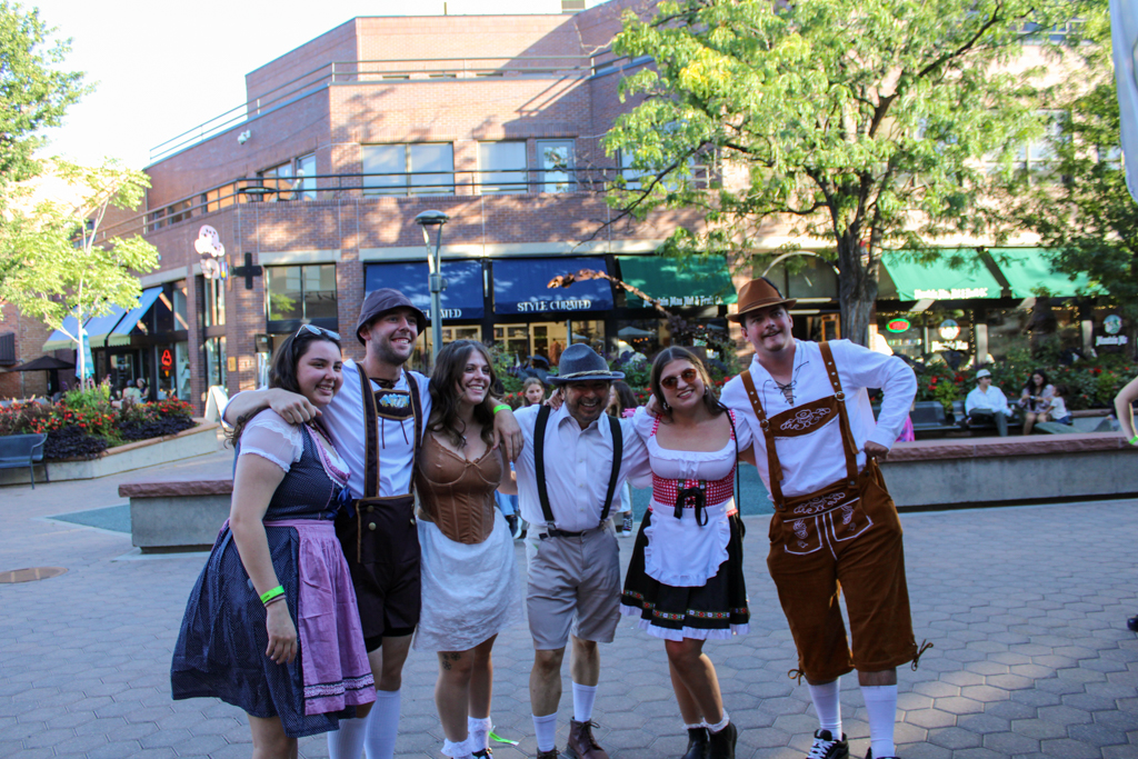 A group of six people wearing traditional Bavarian attire pose for a picture in front of a bar.