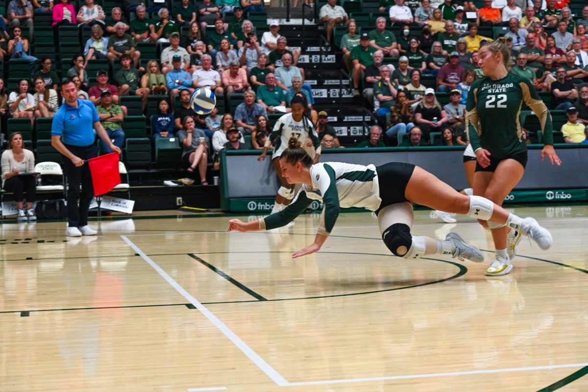 A girl in a long sleeve green and white uniform with black shorts in a diving position on the court