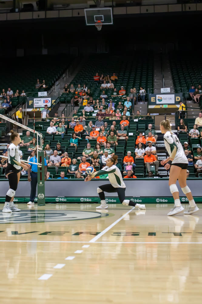 A women's volleyball player gets low to the ground while hitting the ball during a game.