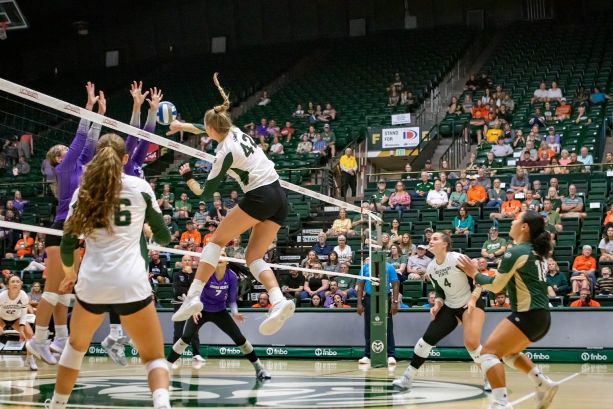 A woman's volleyball player jumps while hitting a ball over the net while her teammates watch around her