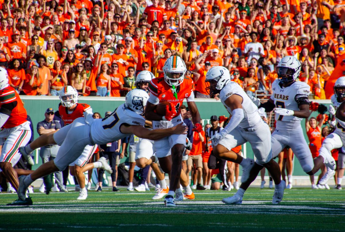 A football player in a bright orange uniform runs with a football while surrounded by football players in white uniforms.