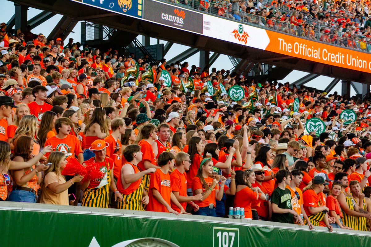 People wearing bright orange and yellow clothes stand in the bleachers of a football stadium.