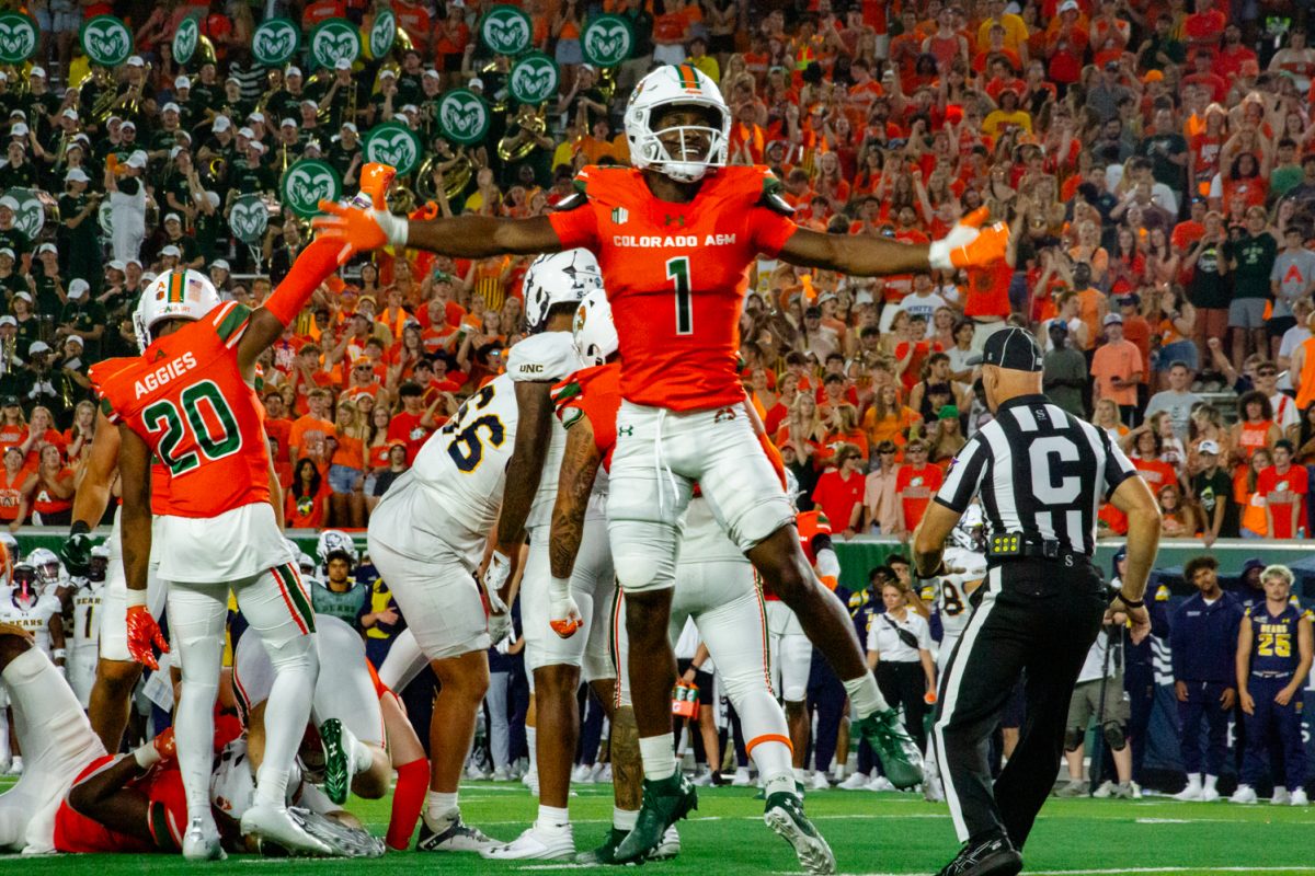 A football player wearing a bright orange uniform jumps in the air and raises his arms as a crowd cheers on players behind him.