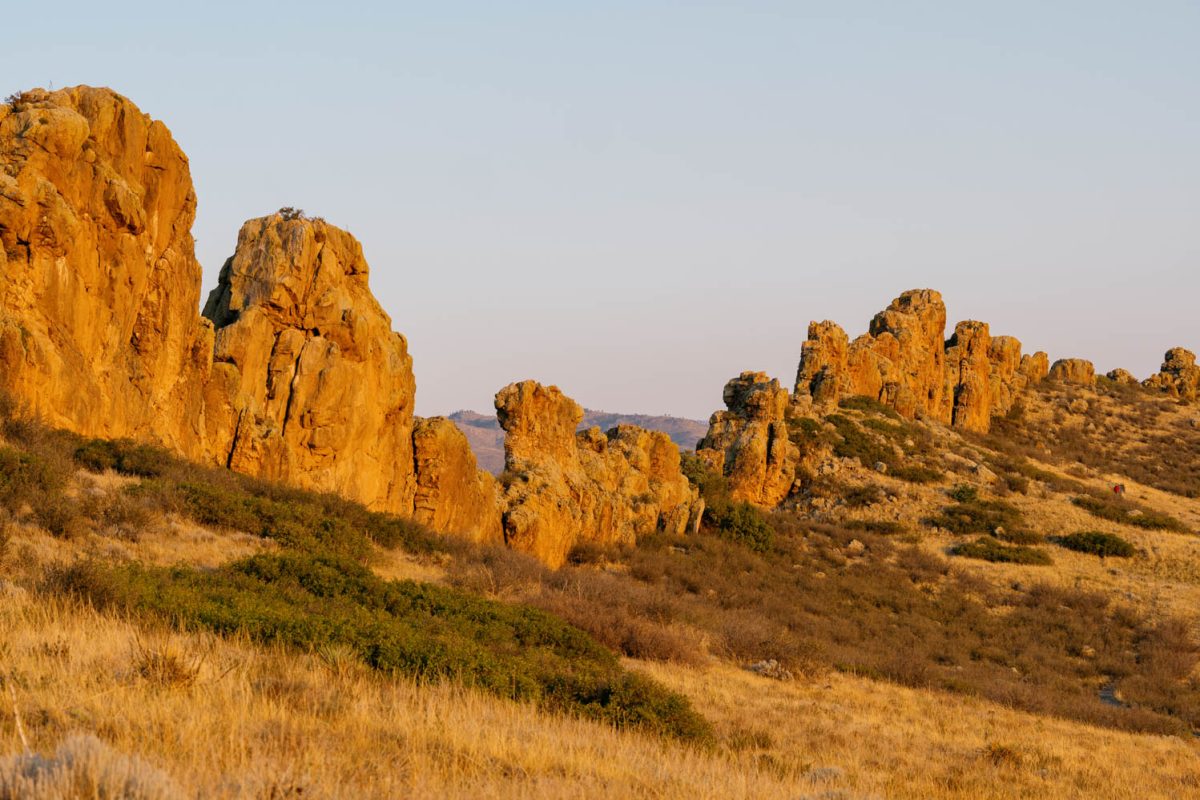 Vertical rock formations at sunrise surrounded by green and pale yellow grasses and vegetation.