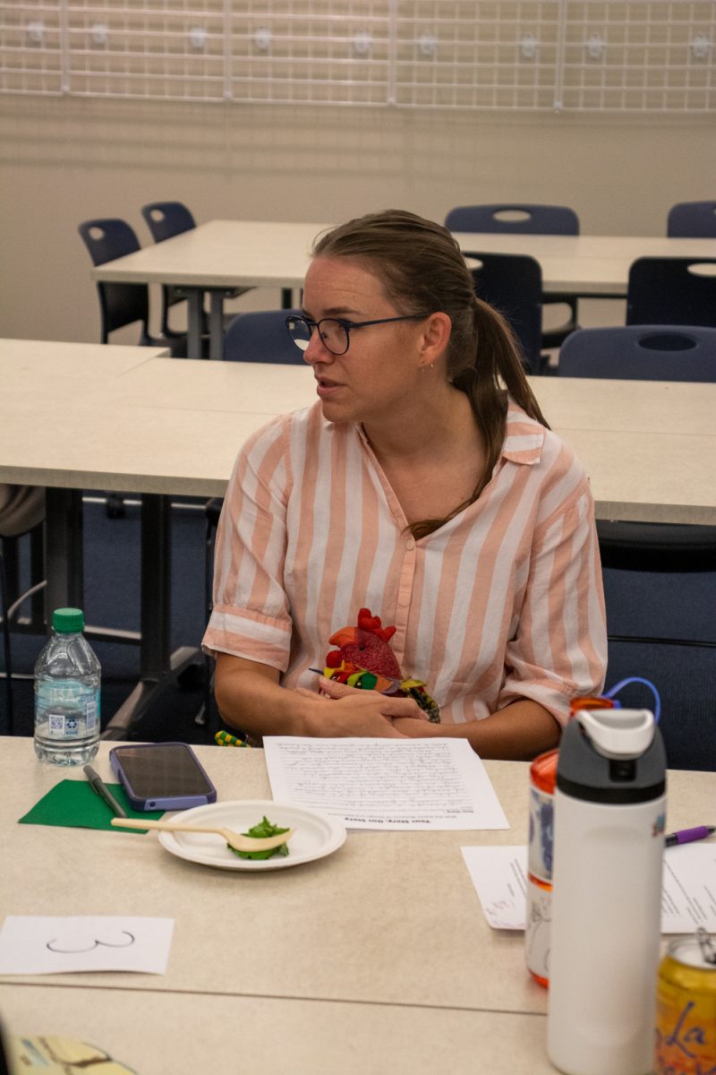 A woman sits at a table holding a fabric chicken.