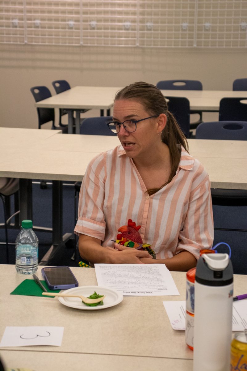 A woman sits at a table while talking and holding a fabric chicken.