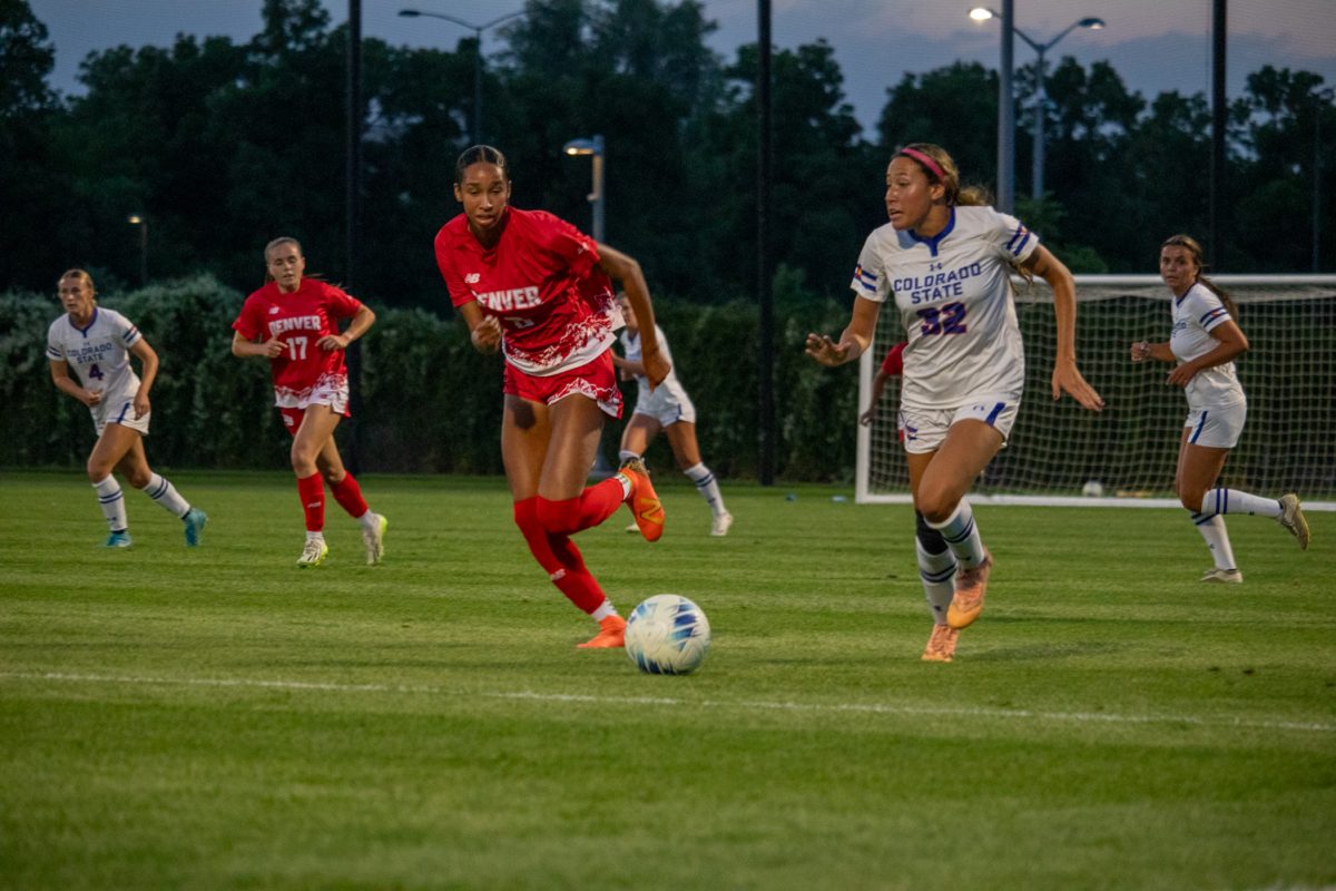 Two soccer players chase a ball downfield.