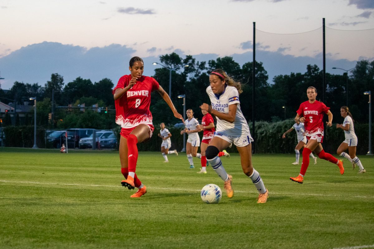 A soccer player kicks a ball while another player defends her.