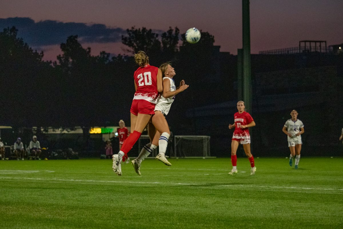 Two players jump in the air trying to head a soccer ball.