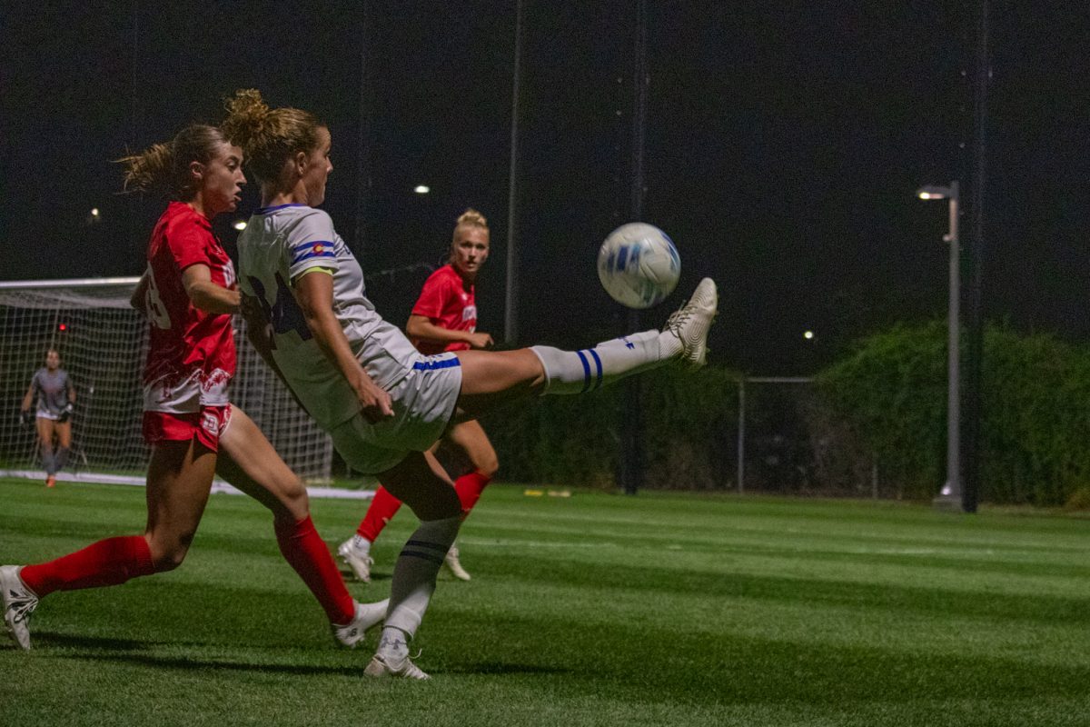 A soccer player stretches to kick a ball in the air.