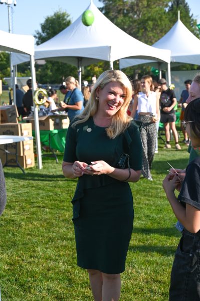 A blond woman in a green dress speaks to a group of people