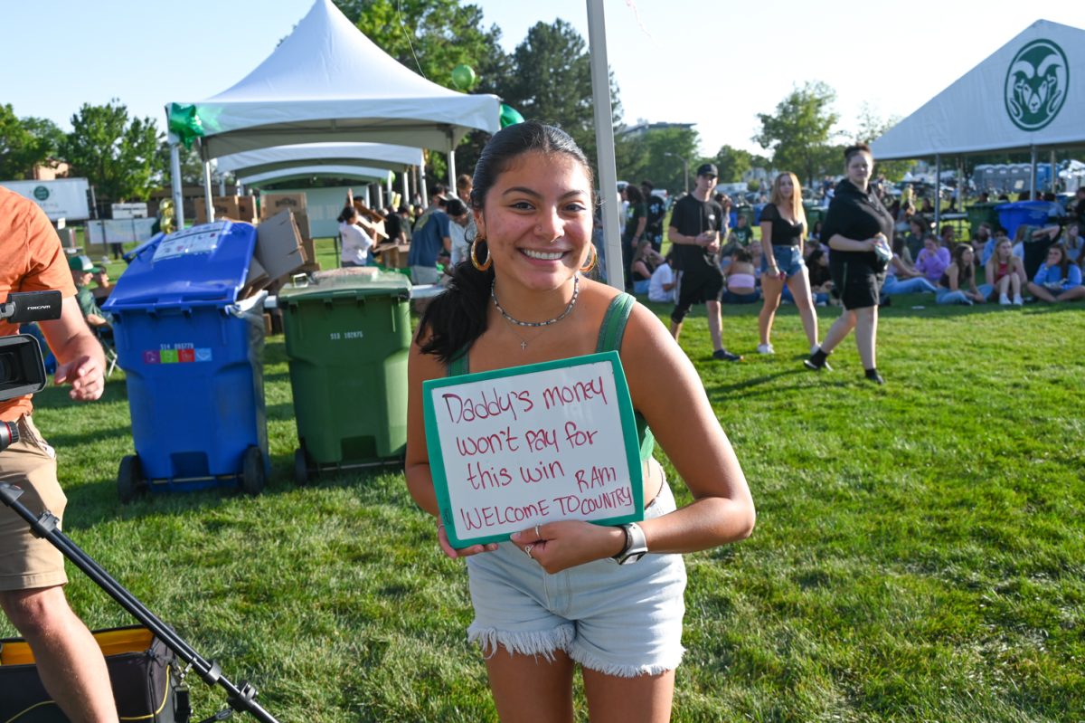 A girl in a green tank top and denim shorts holds up a small whiteboard