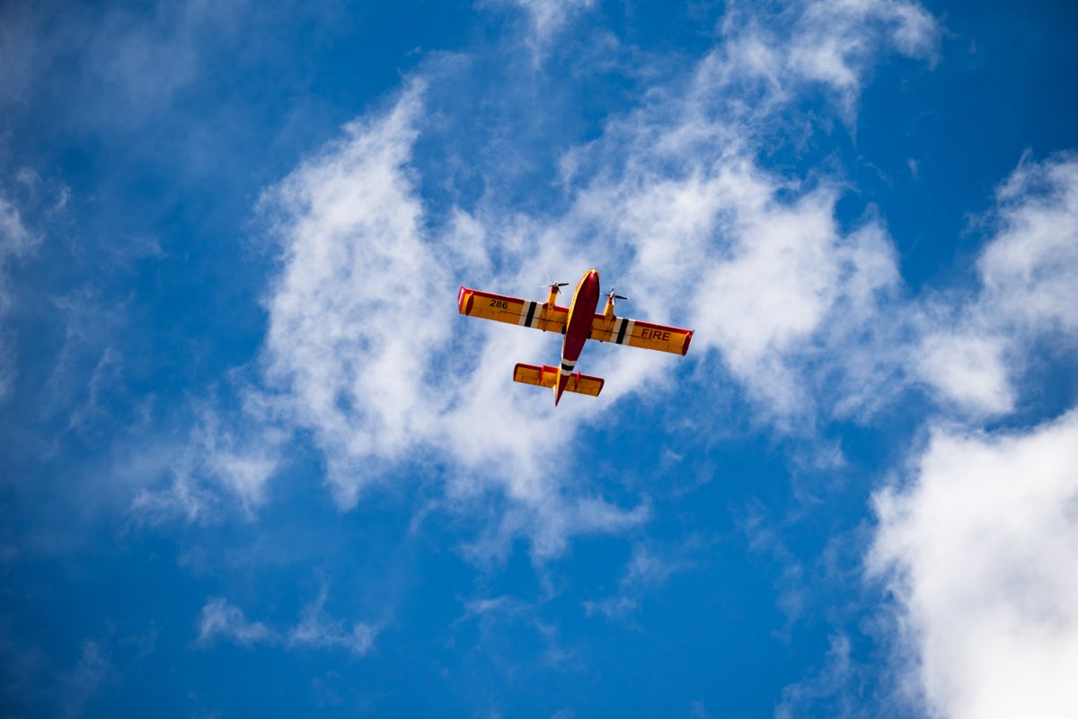 The underside of a yellow and red plane in a blue sky. The right wing reads, "fire."