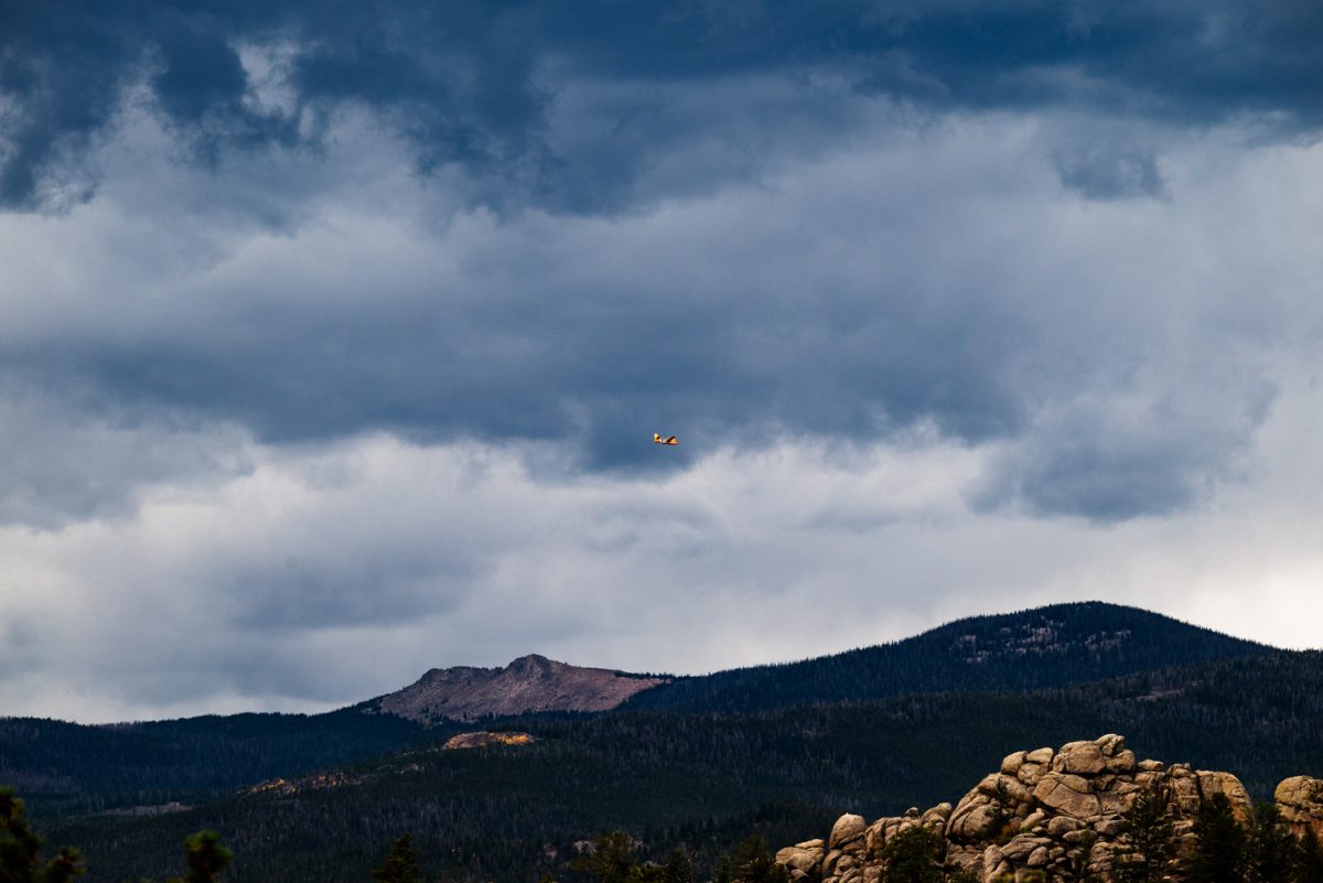 A yellow plane from a distance against a dark blue sky and mountains.