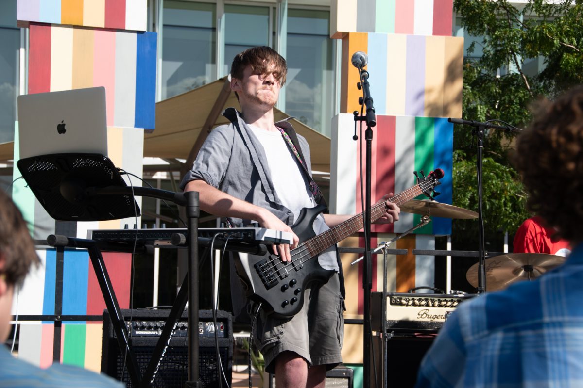 man in front of mic on a stage holding a bass guitar making a face