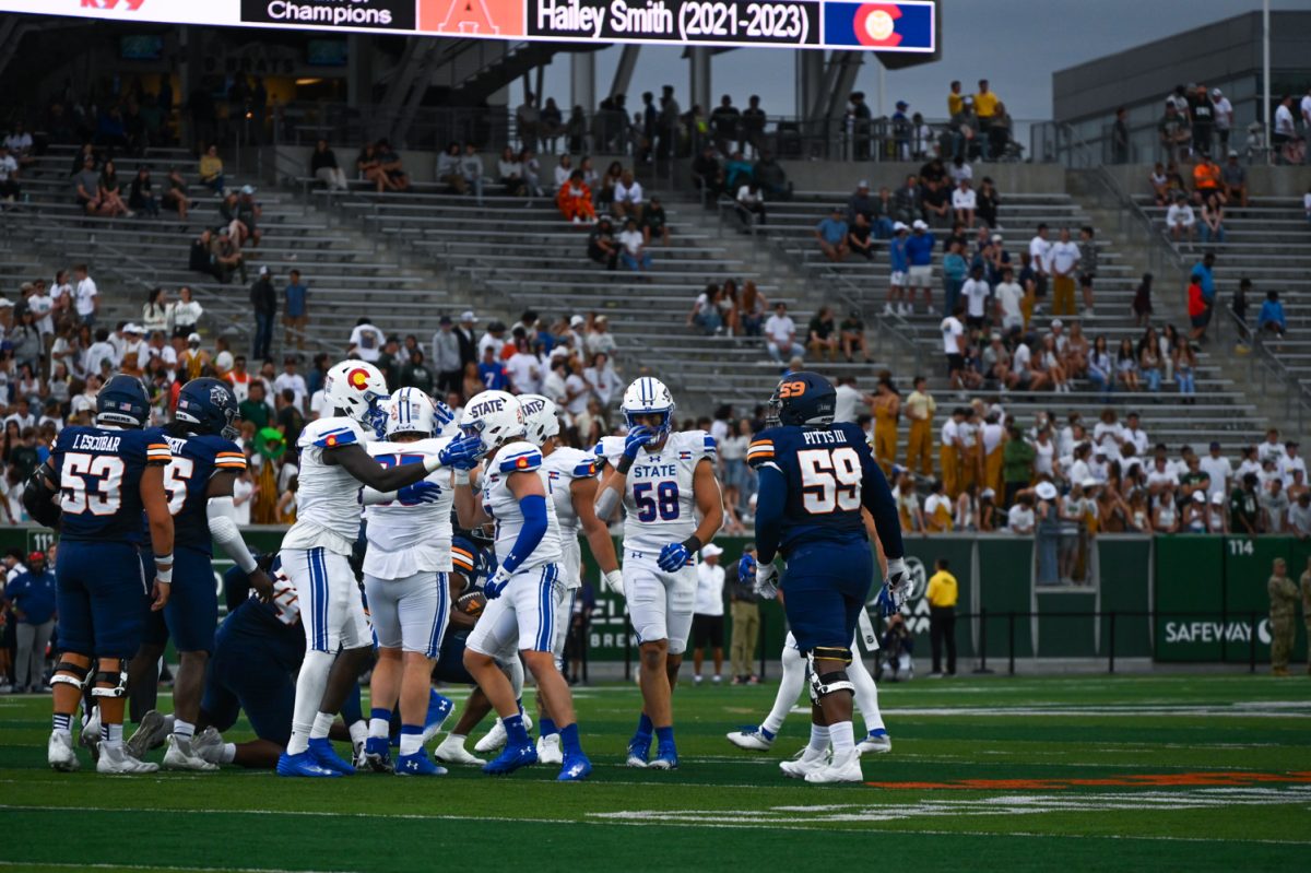 A group of football players in royal blue and white stand on the football field.