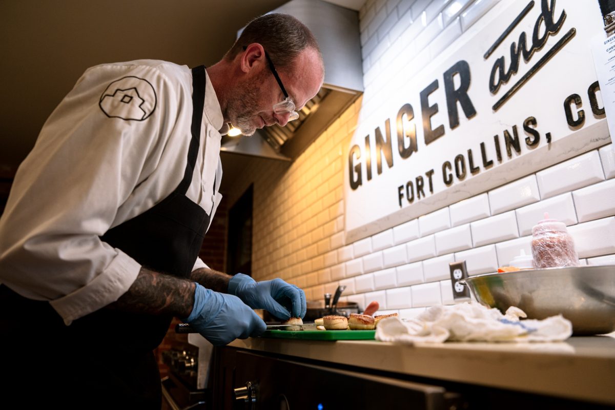 A man with glasses in a white chef's coat and black apron slices scallops.