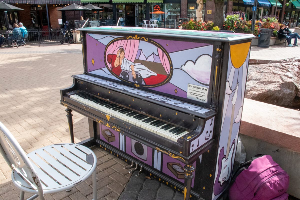 A painted piano sits with a chair in a town square.