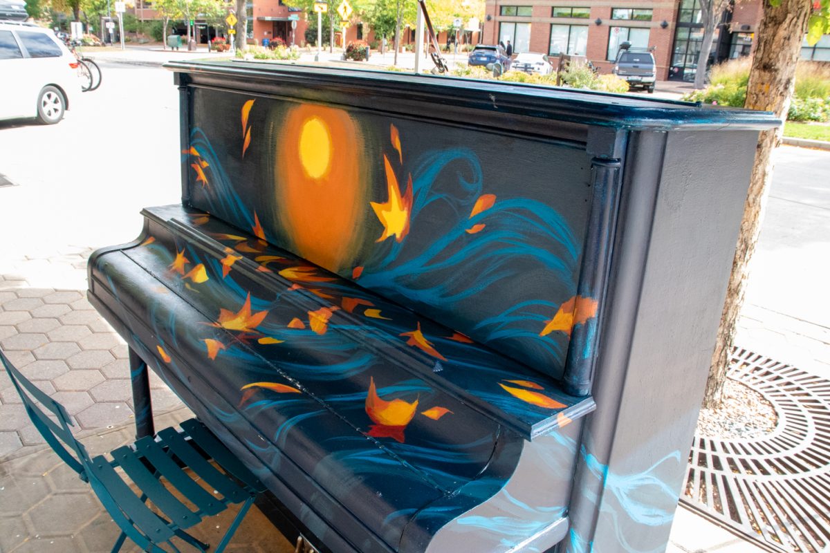 A piano that is being in the middle of being painted sits under a tent in front of a street.