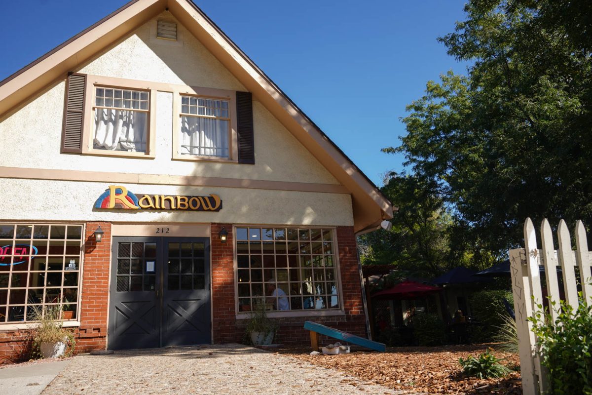 A brick building with blue doors and big windows reading Rainbow above the doors.