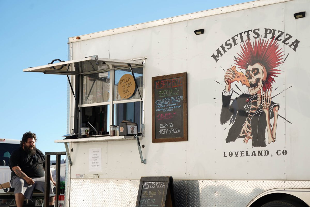 A white food truck with a chalkboard menu and a drawing of a punk skeleton with a red mohawk with the words Misfits Pizza.