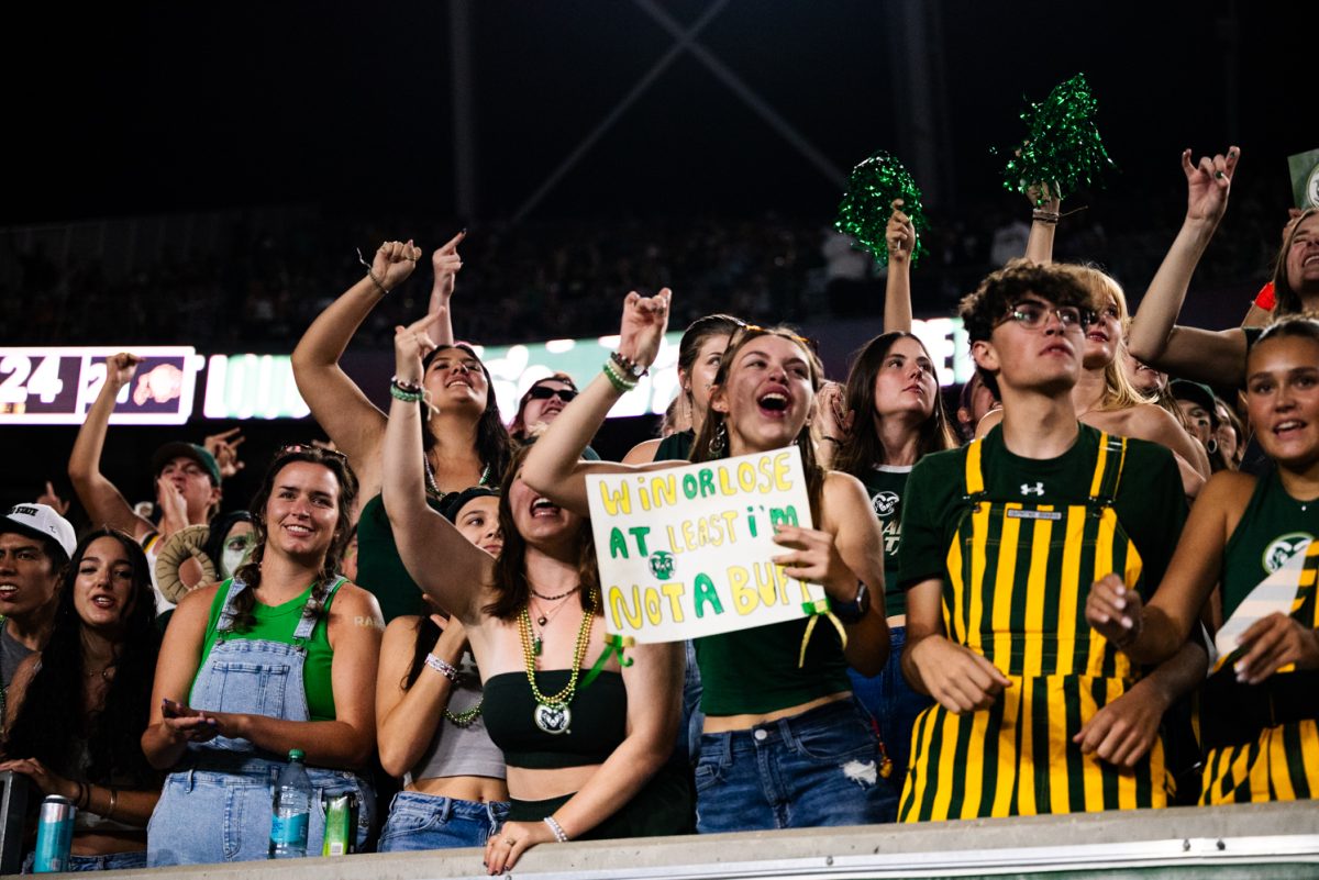 A crowd of cheering students in green and yellow. One of them holds a sign that says, Win or lose, at least I'm not a buff.