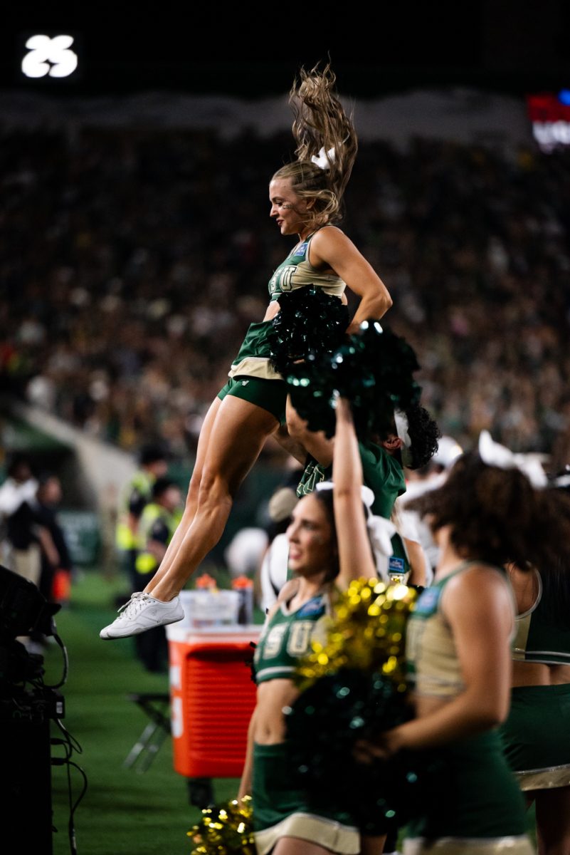 A cheerleader in green and gold is caught by other cheerleaders after being thrown for a stunt.