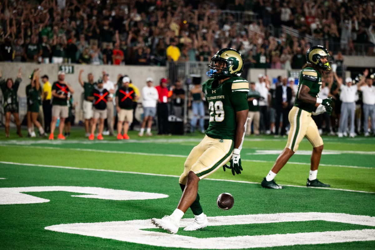 A football player in green and gold drops the football he was holding behind him and dances in the end zone.