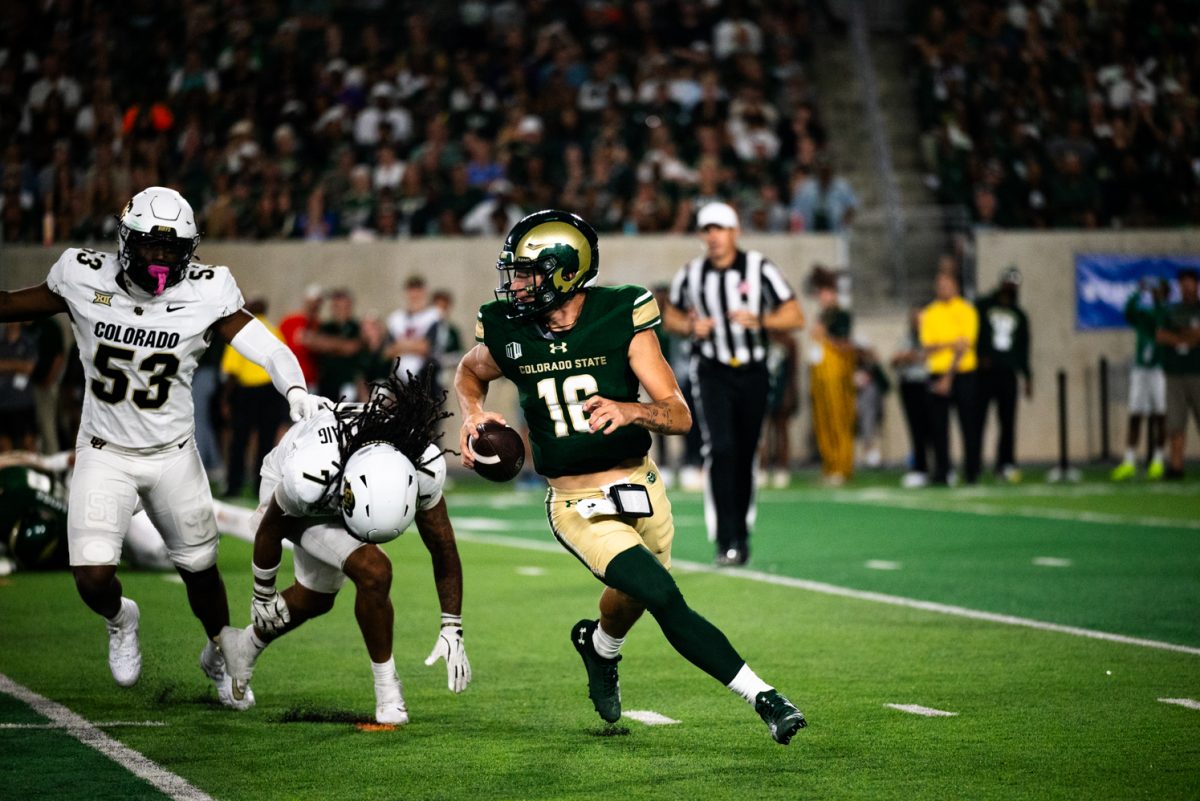 A football player in green and gold runs with a football followed by two football players in white.