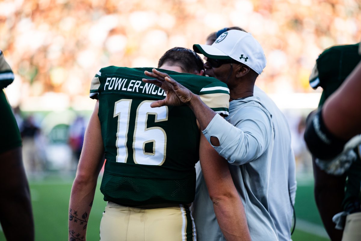 A football player in green and gold leans on the shoulder of a man in a white hat while listening to him speak.