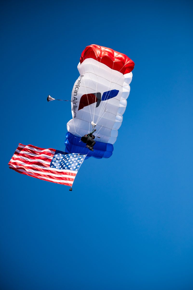A red, white and blue paraglider with an American flag beneath them.