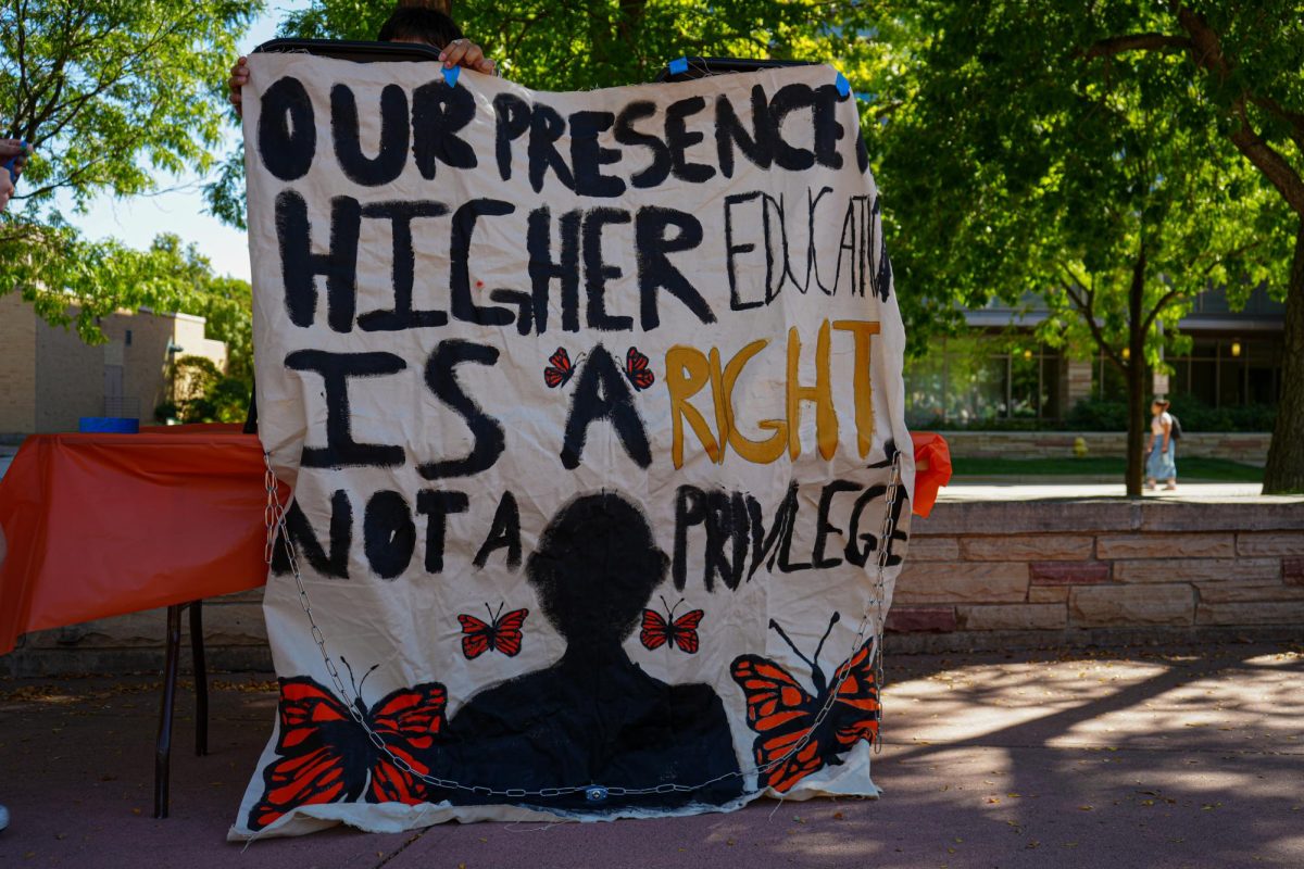 A large, roughly written fabric poster reading, our presence higher education is a right, not a privilege, with orange and black butterflies and a black silhouette of a person.