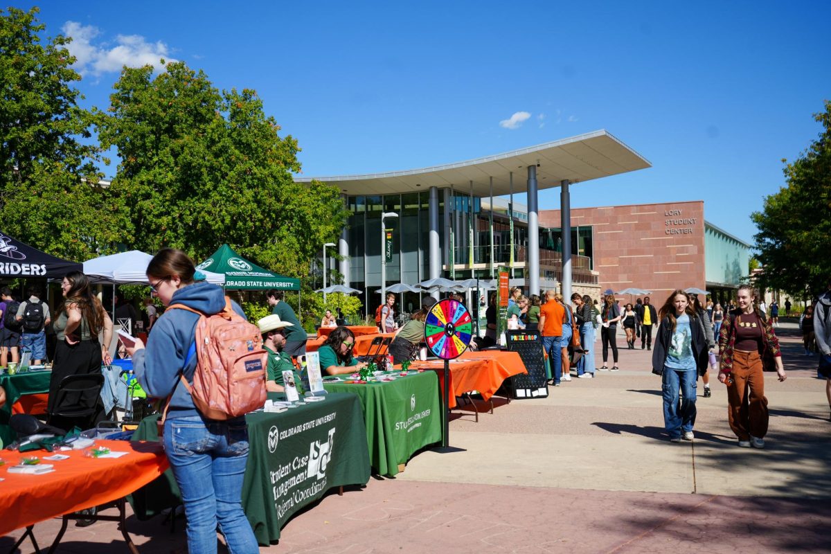 Tables with dark green, light green and orange tablecloths sit in front of the Lory Student Center. Each table has different activities for passersby.