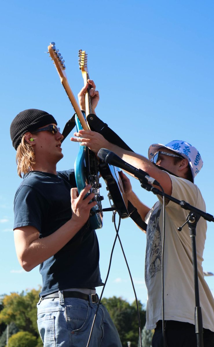 Two men hold guitars in the air and tap them together.