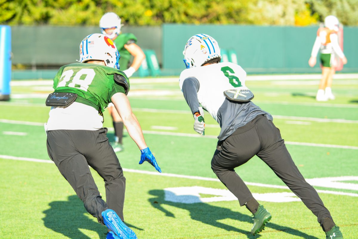 Two CSU football players running a drill where one has the ball, and the other is trying to catch up to him. 