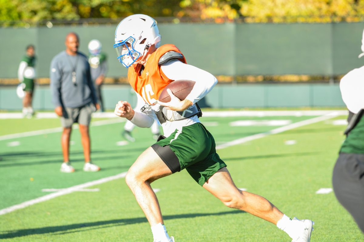 CSU player taking the ball down the field while the coach is watching during morning practice.