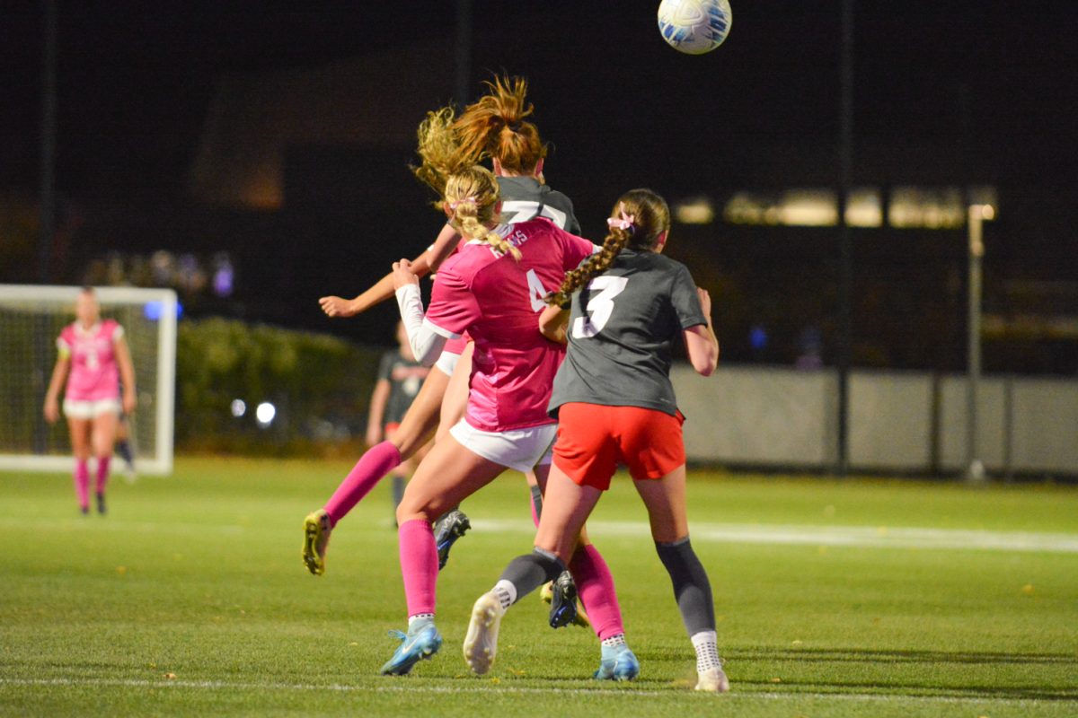 Three soccer players and a ball in the air.