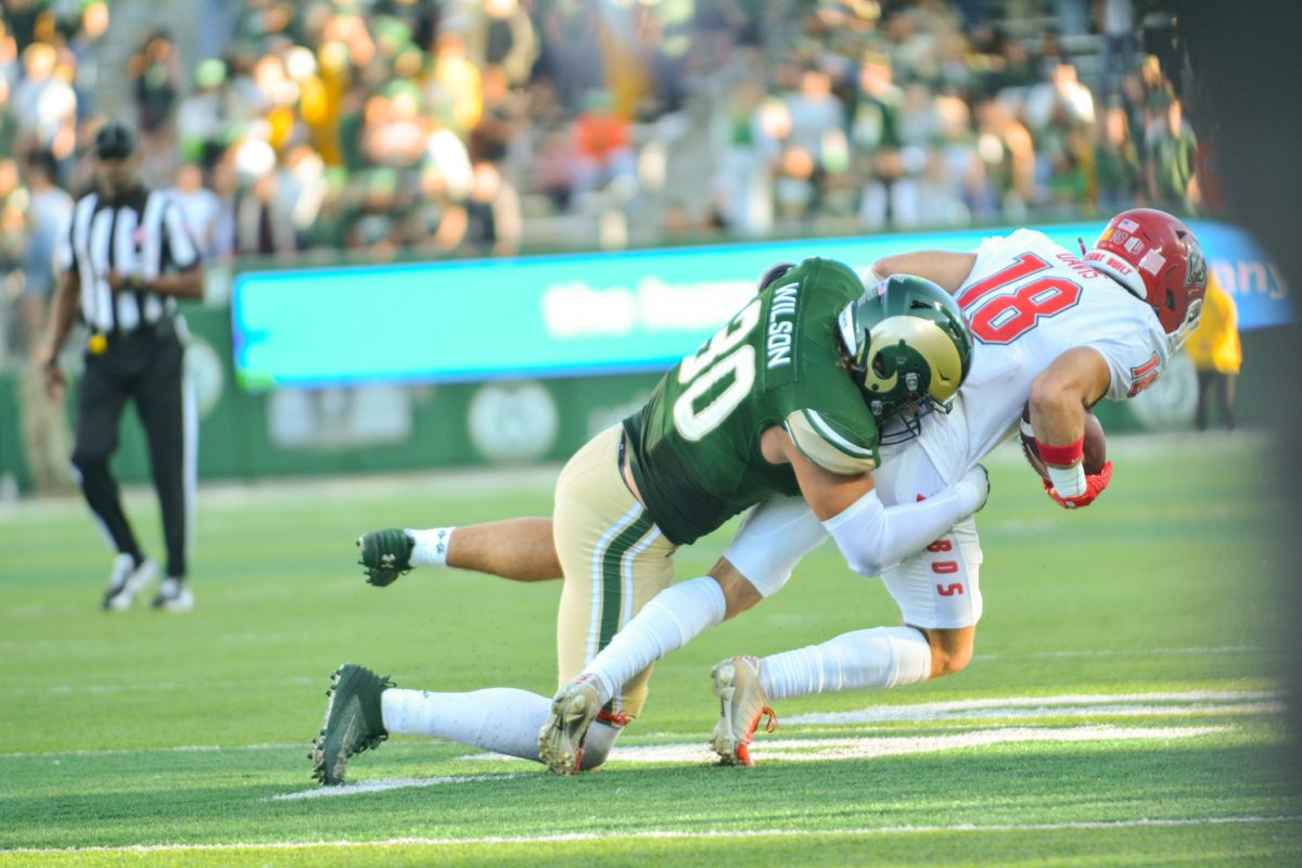 Football player in green jersey tackles player in white jersey