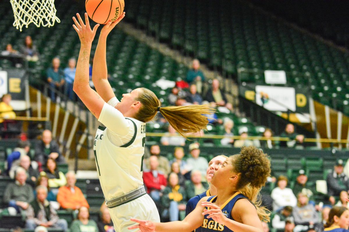 A girl in a green and white jersey throwing the ball into the hoop