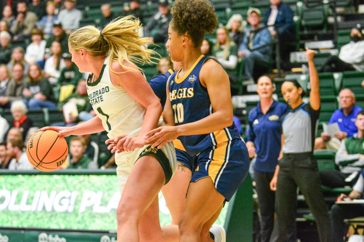 Girl in green and white jersey in front of two players in a blue and gold jerseys.