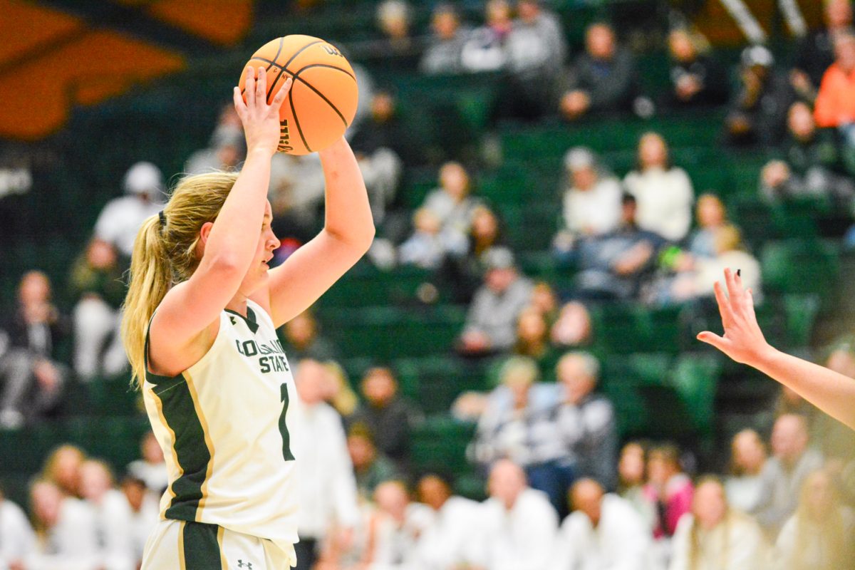 A player in a white and green jersey holding a basketball above her head.