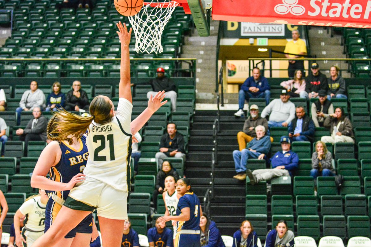 A girl in a green and white jersey jumping up throwing the basketball in the basket