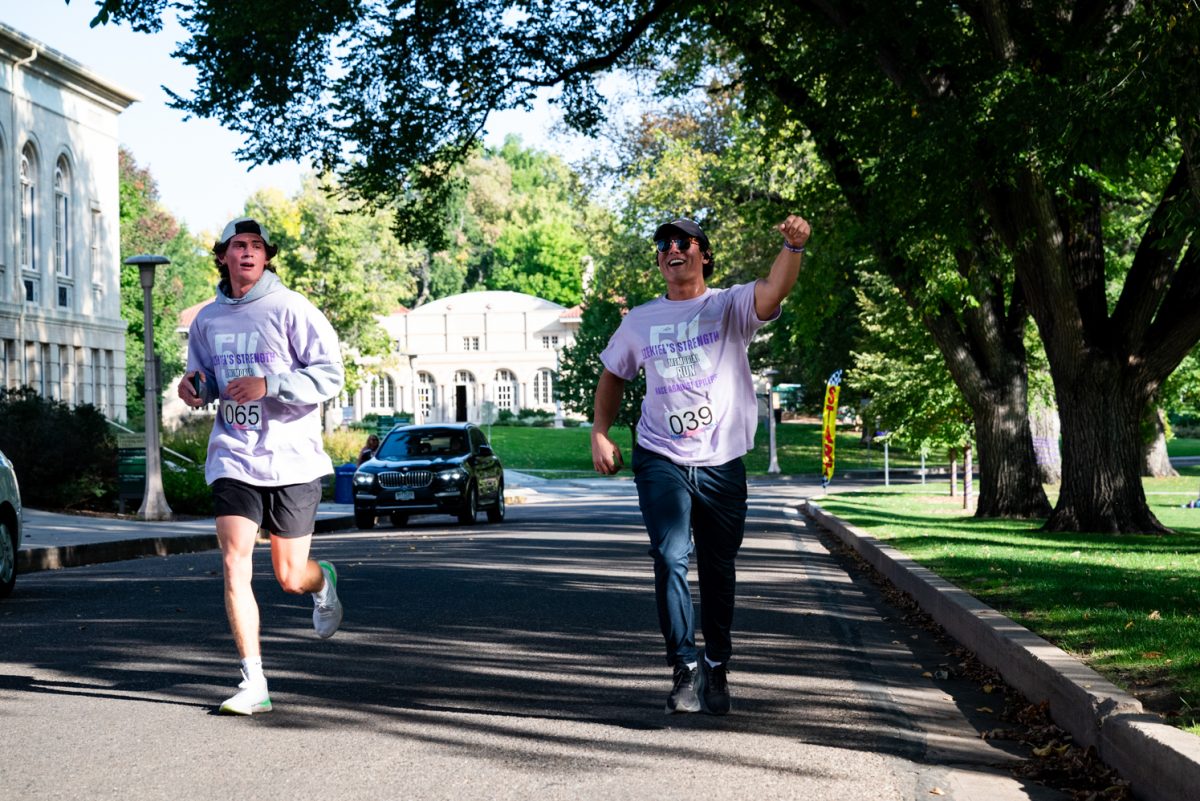 Two men run down a road shaded by trees.